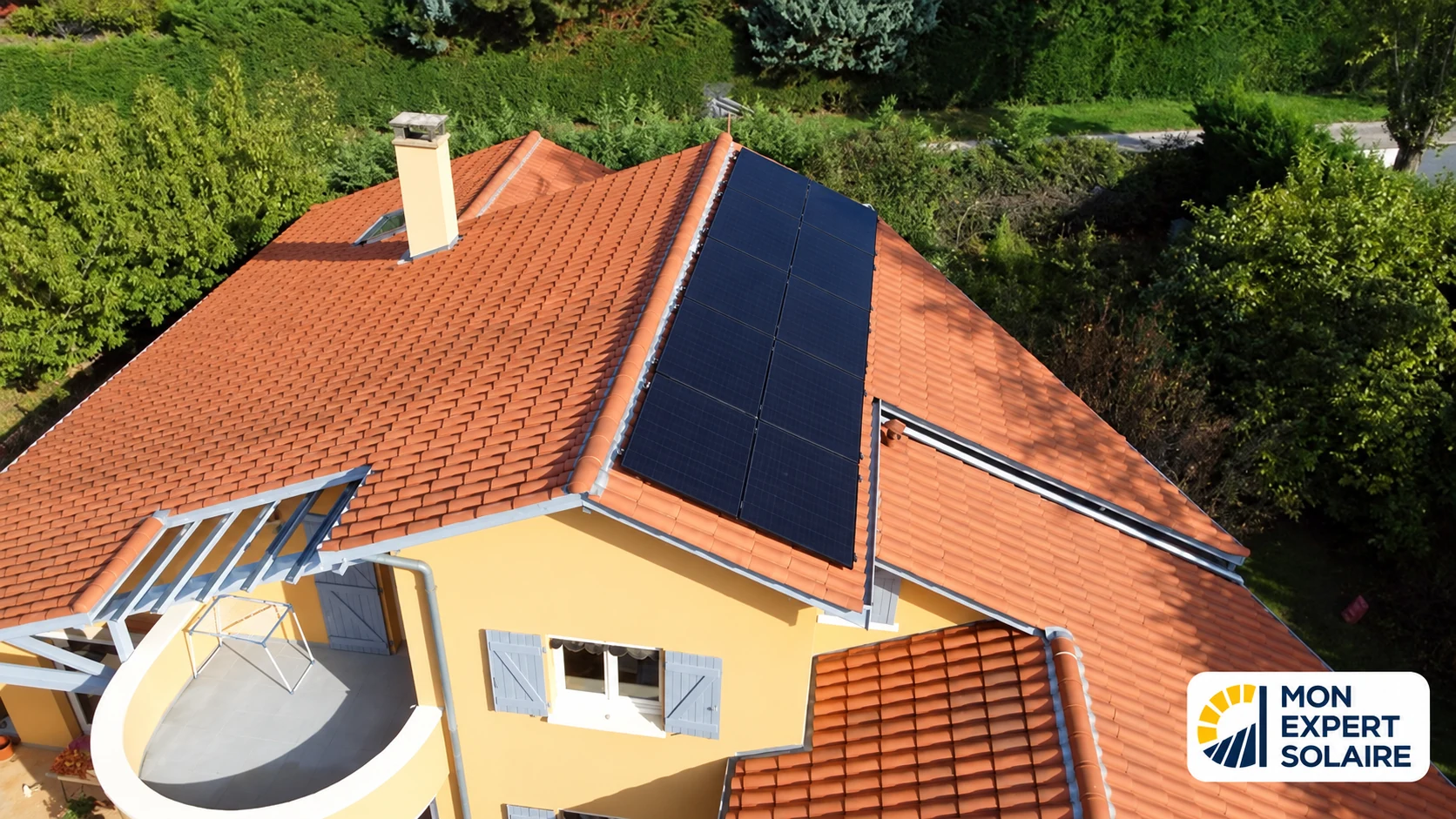Vue aérienne d’une maison aux tuiles orange équipée de panneaux solaires noirs.