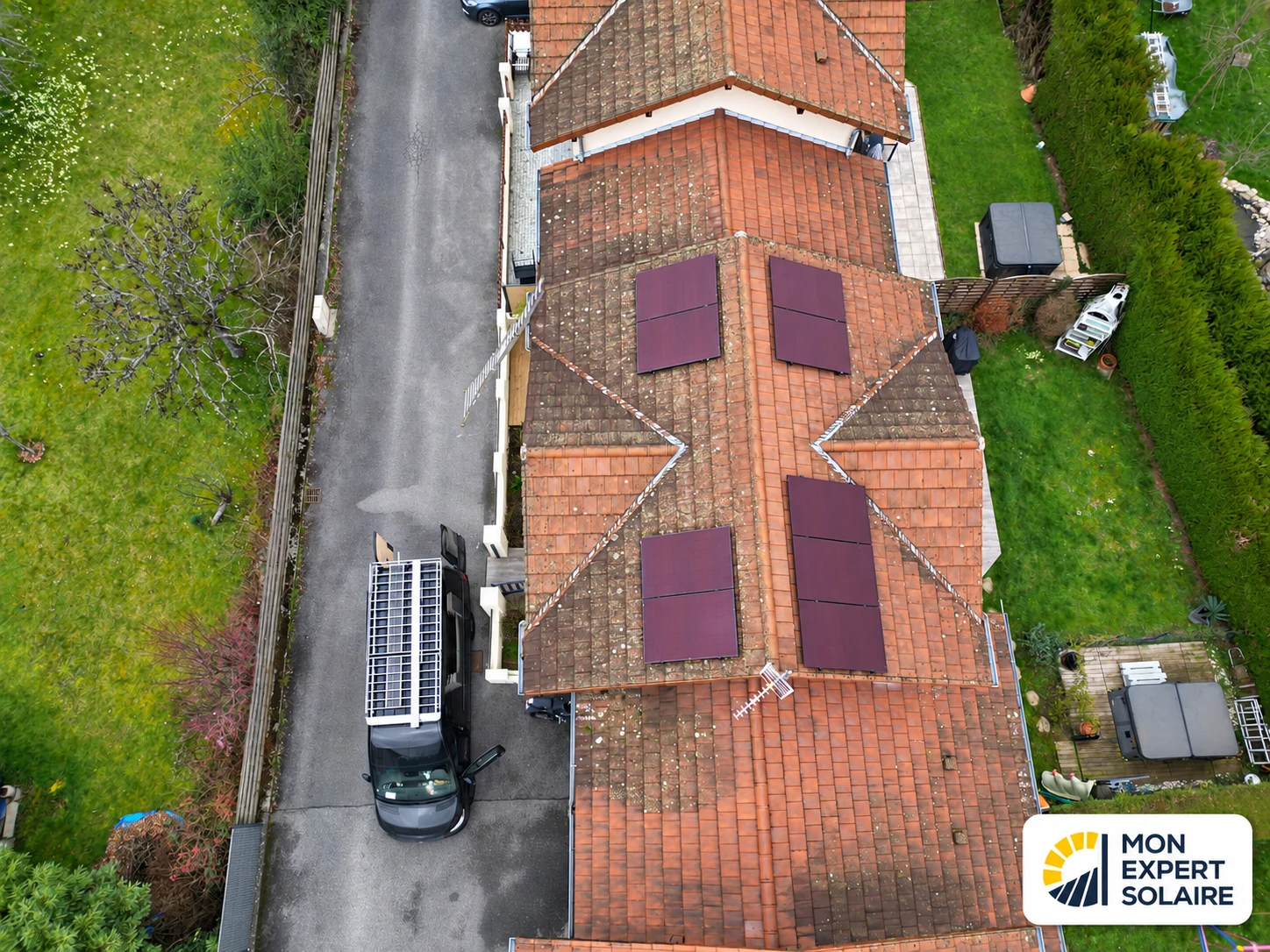 Vue aérienne de panneaux photovoltaïques rouges répartis sur les deux côtés d’une toiture en tuiles.